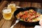 Sausages fried in cast iron skillet with two beer mugs