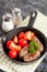 Sausages in a frying pan on black background. Fresh tomate and p