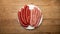 Sausages and merguez arranged in a white plate, on a woody background