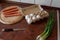 Sausages in polyamide casings. Four sausages lie on a round cutting board. A bunch of green onions. White chicken eggs in a tray.