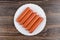 Sausages in polyethylene shell in plate on dark wooden table