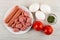 Sausages, slices of sausage in plate, eggs, tomatoes, bowl with parsley on wooden table. Top view