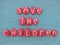 Save the children, unique slogan composed with red colored stone letters over green sand