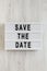 `Save the date` words on a lightbox on a white wooden surface, top view. Overhead, from above, flat lay. Close-up