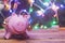 Save money for christmas. Piggy bank with xmas toys on ears against decorated with festive lights christmas tree. Christmas