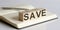 SAVE sign on a wooden block on notebook background