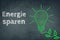 Saving energy, german language, chalkboard, drawing of a green light bulb