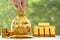 Saving gold, Woman hand putting a coin into piggy bank and gold bar on natural green background,Business investment and Saving