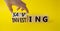Saving and Investing symbol. Hand turns wooden cubes and changes word Investing to Saving. Beautiful yellow background. Business