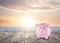 Saving money for summer vacation. Piggy bank on wooden surface near sea at sunset, space for text