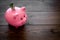 Savings. Moneybox in shape of pig with banknotes falling into it on dark wooden background space for text