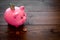 Savings. Moneybox in shape of pig with banknotes falling into it near coins on dark wooden background copy space
