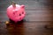 Savings. Moneybox in shape of pig with banknotes falling into it near coins on dark wooden background copy space
