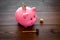 Savings. Moneybox in shape of pig with banknotes falling into it near coins and hammer on dark wooden background copy