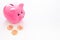 Savings. Moneybox in shape of pig near coins on white background copy space