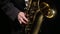 Saxophonist plays with fingers on the saxophone valves in a dark studio, close-up. Musician is a man playing with hands