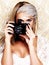 Say cheese. A glamourous young woman in retro attire holding a camera while posing against a paisley background.