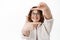 Say cheese. Happy authentic young woman in glasses, looking through hand photo frames gesture and smiling with white