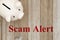 Scam Alert message with piggy bank on weathered wood