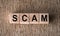 SCAM word written on wooden blocks on a brown background