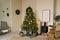 Scandinavian beige Christmas interior with decorated Christmas tree. Fireplace with armchair, wreath on the wall and gifts under