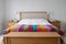 Scandinavian inspired bedroom interior showing wooden bedroom furniture, white painted walls, white bedding and colourful blanket