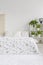 Scandinavian style bedroom interior with green plants pattern on white bedding lying on a bed. Fluffy rug on the floor. Empty wall