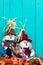 Scarecrows sitting by fall decor by teal blue wooden fence