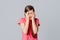 Scared anxious young girl amazed shocked hands cover face, wear in casual pink t shirt, standing over gray background. Young
