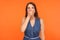 Scared brunette woman in denim dress covering mouth with hand and looking frightened at camera