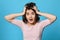 scared curly young brunette woman on blue background.