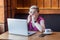 Scared! Portrait of emotional nervous young girl with blonde short hear in pink t-shirt and eyeglasses is sitting in cafe, working