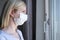 Scared woman in surgical face mask staying at home and looking through the window, covid-19 quarantine and self isolation,