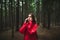Scared young female tourist in red raincoat is lost in forest calling someone on the phone, touching her face. Terrified traveler
