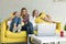 Scared young lesbian couple with daughters in casual clothes sitting together on yellow sofa at home, exited family