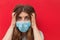 Scared young woman in medical mask standing over red background.