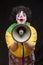 Scary clown shouting into a megaphone on a black background