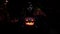 Scary creepy hooded man figure holds jack o lantern carved pumpkin standing in dark alley