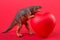 Scary dinosaur toy grabbed a red heart, the concept of illness and early diagnosis