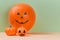 Scary faces on air balloon and decorative pumpkin. Halloween and autumn holiday. Copy space. Isolated on green backdrop