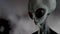 Scary gray alien stands and looks blinking on a dark smoky background. UFO futuristic concept. 3D rendering.