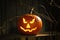 Scary jack o`lantern pumpkin on wooden bench in darkness. Halloween decor