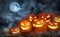 Scary Jack O Lantern pumpkins surrounded by mystical mist under moon on Halloween