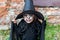 Scary little girl in a witch costume looking at camera with frightening expression on brick wall background. Halloween and day of