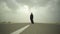 Scary man walks on the desert road, looking for his victim. Maniac in a black cloak is walking under frightening sky