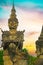 Scary mythological hindu mystic creature stone sculpture and buddha head, dramatic sunset sky, palm trees- Buddha Park Wat Xieng