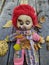 scary and old battered clown doll with burnt face and red hair on the background of old wooden board with autumn leaves