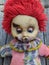 scary and old battered clown doll with burnt face and red hair on the background of old wooden board with autumn leaves