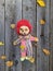 scary and old battered clown doll with burnt face and red hair on the background of old wooden board with autumn leaves