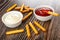 Scattered bread sticks, bowl with mayonnaise, breadstick in bowl with ketchup on table